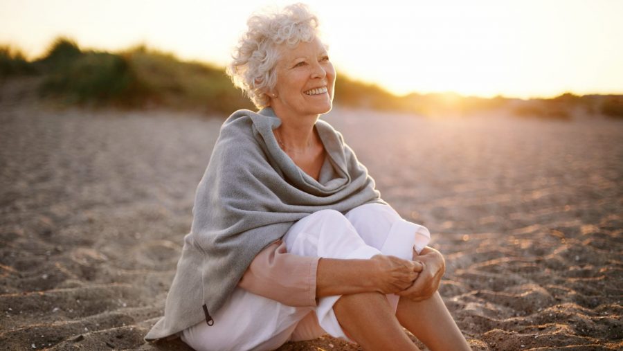 Happy retired woman wearing shawl sitting relaxed on the sand