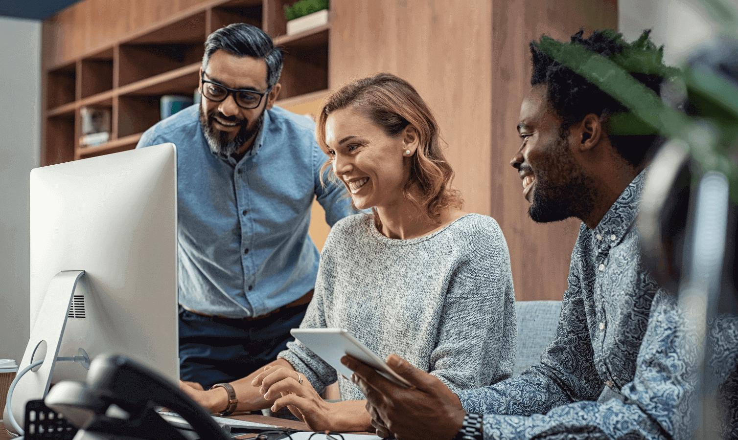 3 work colleagues gathered around 1 desk smiling.