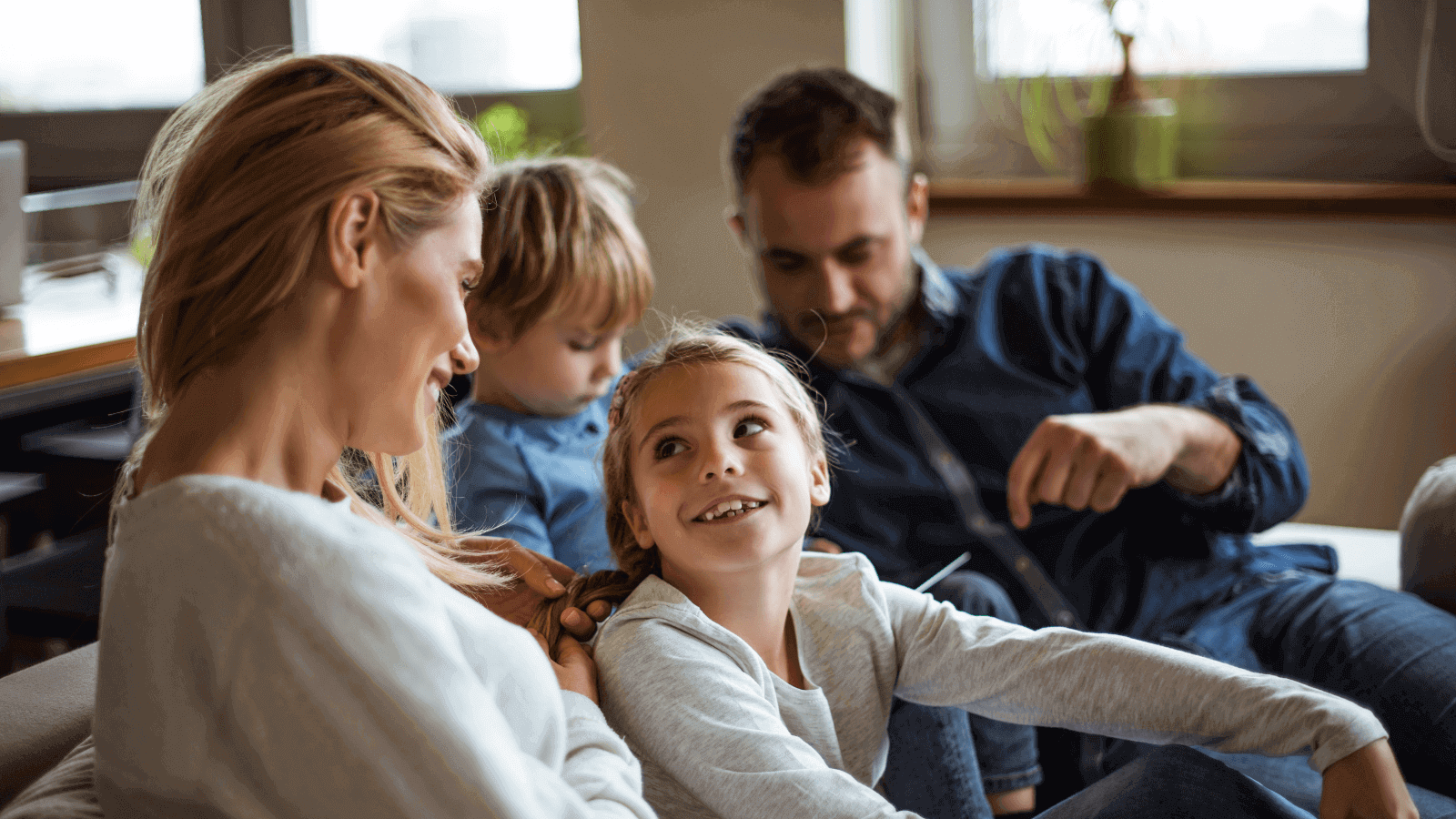 A family sat on a sofa together, mum plaiting girls hair.